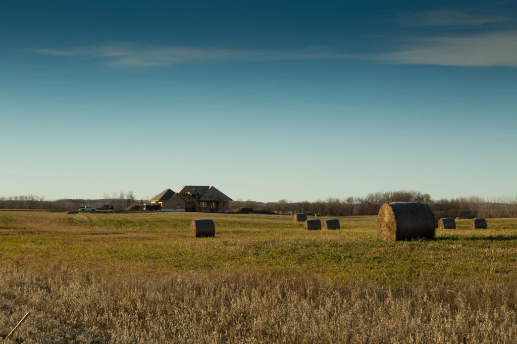 Hay bales on open prairie beside Brylee Estates with homes in the distance